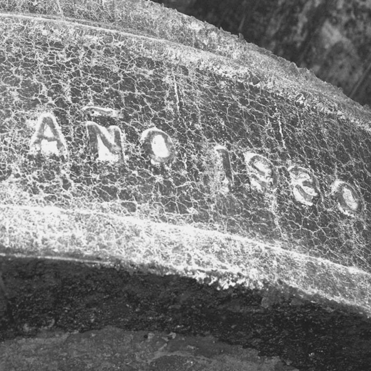 Primo piano di un'antica incisione su pietra, segnata dal tempo, con caratteri scolpiti visibili sulla superficie screpolata. L'immagine evoca tradizione, storia e il legame ancestrale con la produzione dell'olio extravergine d'oliva Verde Esmeralda.